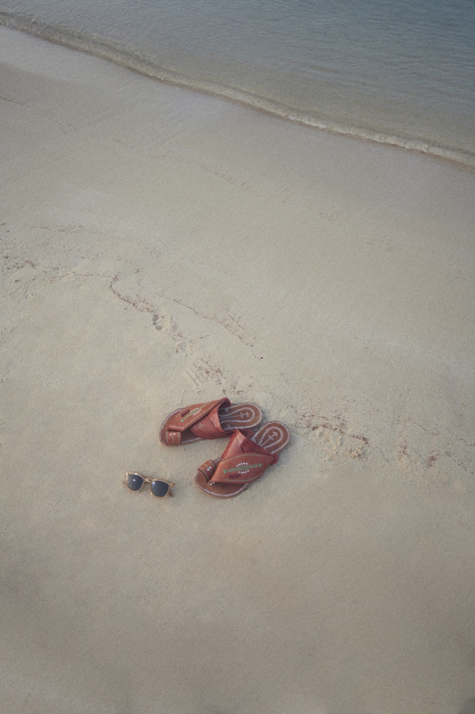 Sandals and sunglasses on white sand